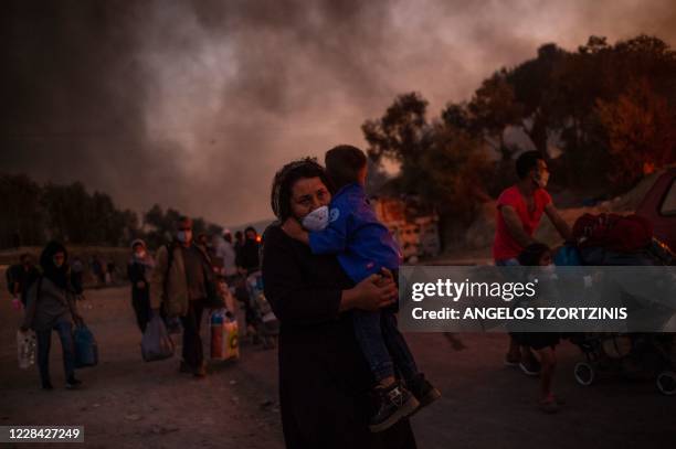 Woman carries a child as they leave after a major fire broke out in the Moria migrants camp on the Greek Aegean island of Lesbos, on September 9,...