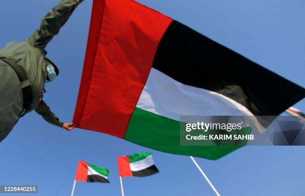 An Emirati policeman wearing a protective mask amid the COVID-19 pandemic, unfurls a national flag at the beach in Dubai in the United Arab Emirates,...