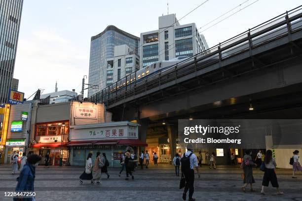 Pedestrians walk near Yurakucho station as a Shinkansen bullet train travels along a track track in Tokyo, Japan, on Thursday, Sept. 3, 2020. In...