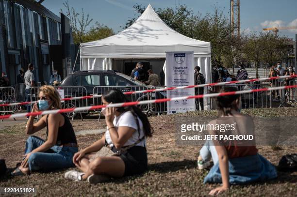 People sit on the ground as they queue to get tested for Covid-19, on September 11, 2020 in Venissieux, near Lyon, amid the novel coronavirus...