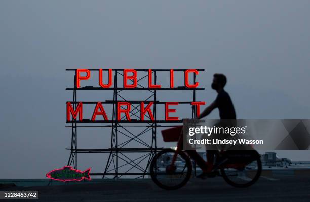 Wildfire smoke obscures the view of Elliott Bay as a person bikes past a Pike Place Market sign on September 11, 2020 in Seattle, Washington....