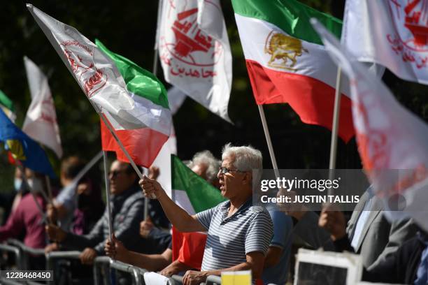 Protesters wave the Lion and Sun flag of the National Council of Resistance of Iran and the white flag of the People's Mujahedin of Iran, two Iranian...