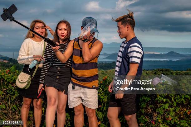 Local tourists remove their face masks and face shields to take pictures with a view of Taal Volcano on September 13, 2020 in Tagaytay, Cavite...
