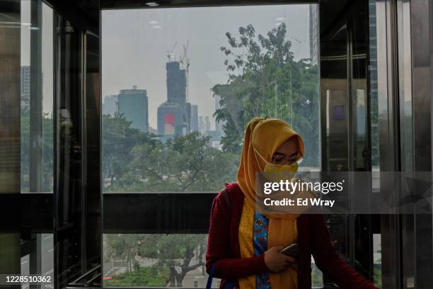An Indonesian woman wearing a facemark rides a glass walled elevator in the central business district September 14, 2020 in Jakarta, Indonesia....