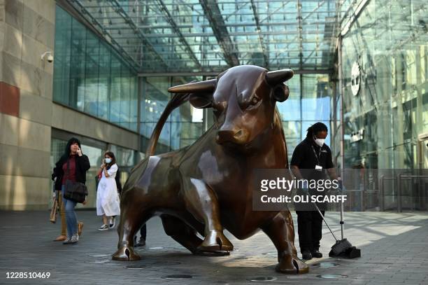 Worker wearing a face mask or covering due to the COVID-19 pandemic, sweeps the floor near a statue of a bull at the Bullring in Birmingham, central...
