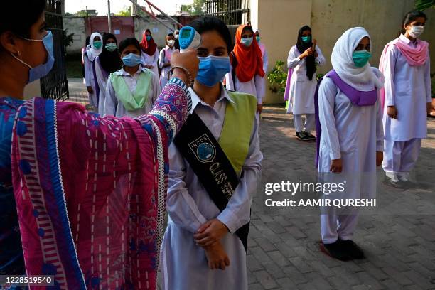 Teacher checks the body temperature of students at the entrance of the Islamabad Model College of Commerce for Girls in Islamabad on September 15,...
