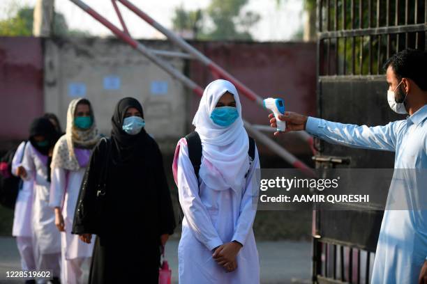Staff member checks the body temperature of students at the entrance of the Islamabad Model College of Commerce for Girls in Islamabad on September...