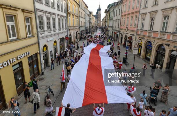 Protesters carrying a giant white, red and white Belarusian flag on Florianska Street in Krakow's Old Town. Members of the local Belarusian diaspora,...