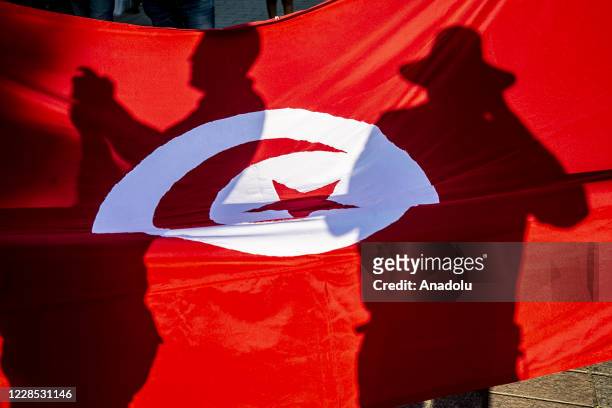 Shadows of Tunisians reflect on a Tunisian flag during a protest against United Arab Emirates' and Bahrain's deal to normalise ties with Israel, at...