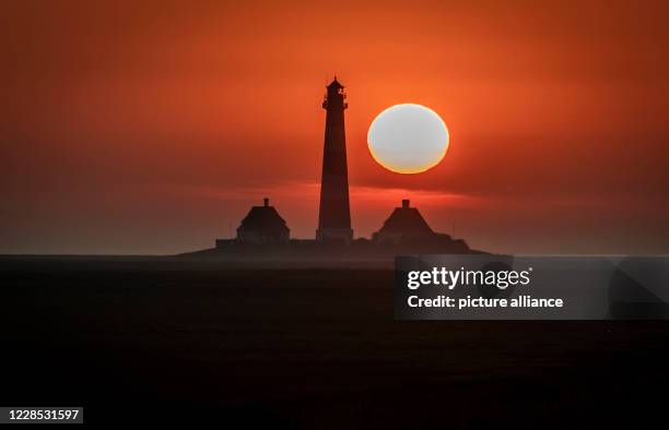 September 2020, Schleswig-Holstein, Westerhever: The sun sets in the evening behind the lighthouse of Westerhever near Saint Peter-Ording on the...