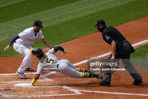 Tony Kemp of the Oakland Athletics touches home plate to score after avoiding the tag by Josh Fuentes of the Colorado Rockies as home plate umpire...