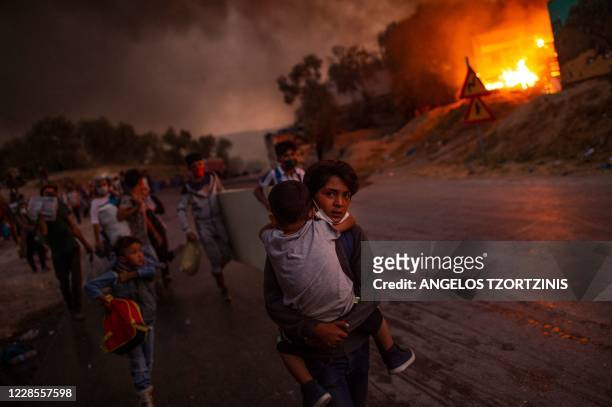 Boy carries a child in his arms as migrants flee the Moria camp after a fire broke out, on the island of Lesbos on September 9, 2020. - Thousands of...