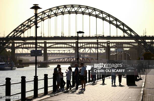 People walk along the quayside, on the banks of the River Tyne, backdropped by the Tyne Bridge in Newcastle, north-east England, on September 17,...