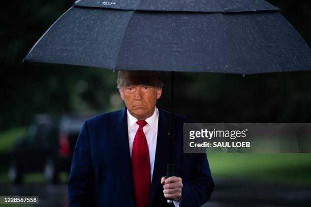 President Donald Trump holds an umbrella as he speaks to the media under the rain prior to departing from the South Lawn of the White House in...