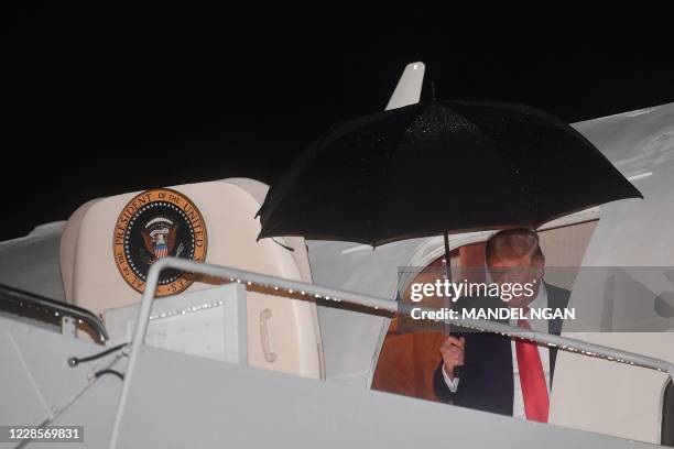 President Donald Trump holds an umbrella as he steps off Air Force One under the rain upon return to Andrews Air Force Base in Maryland early on...