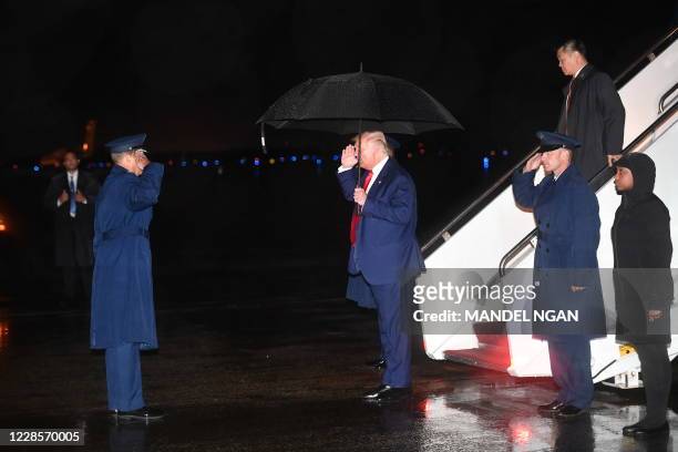 President Donald Trump salutes holding an umbrella under the rain upon return to Andrews Air Force Base in Maryland early on September 18, 2020. -...
