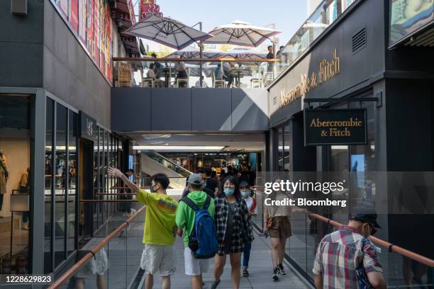 People wearing protective masks walk past an Abercrombie & Fitch Co. Store at a shopping area in Beijing, China on Sunday, Sept. 20, 2020. China's...