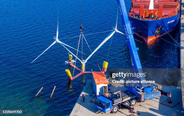 September 2020, Mecklenburg-Western Pomerania, Vierow: A crane lifts a model of a plant with floating wind turbines into the water in the harbour....