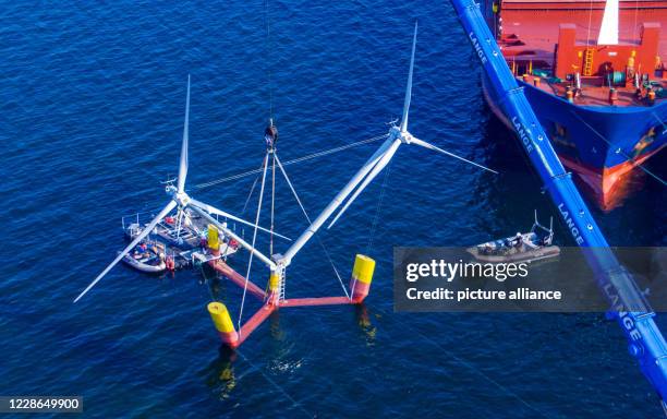 September 2020, Mecklenburg-Western Pomerania, Vierow: A crane lifts a model of a plant with floating wind turbines into the water in the harbour....