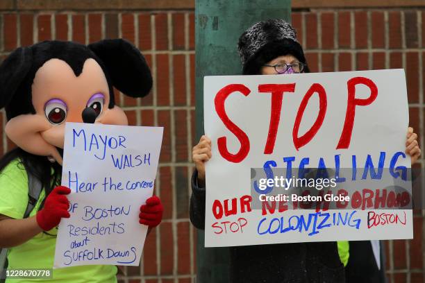 Protester wearing a Mickey Mouse mask and another protester hold signs as the PUEBLO Coalition rallies outside Boston City Hall in Boston, calling...