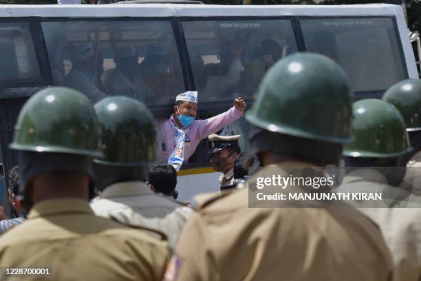 Police personnel stand guard as an activist from a farmers rights organisation gestures during a protest following the recent passing of agriculture...