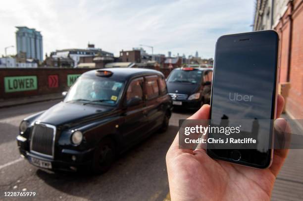 In this photo illustration a phone is held displaying the Uber logo in its app in front of a taxi stand at Waterloo station on September 28, 2020 in...