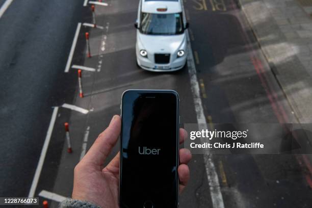 In this photo illustration a phone is held displaying the Uber logo as a taxi pases at Waterloo station on September 28, 2020 in London, England. The...