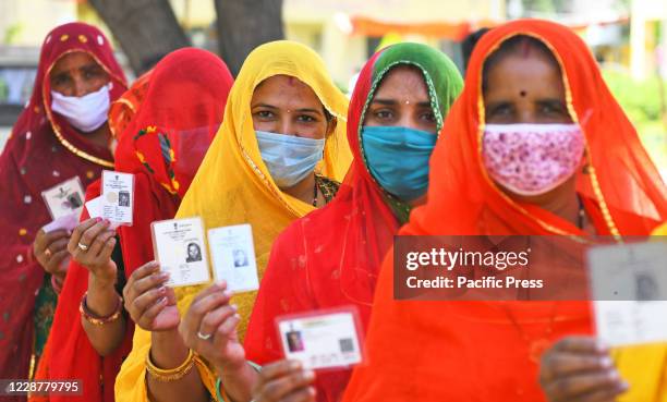 Rajasthani veiled women show their voters ID while waiting in long queues to cast votes at a polling station during Panchayati Raj elections, amid...