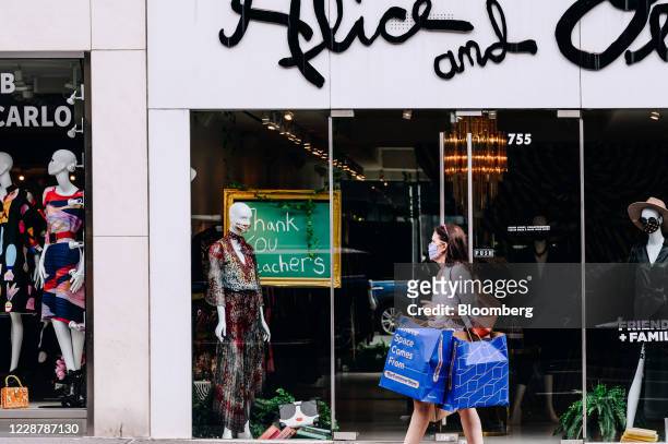 Pedestrian wearing a protective mask carries shopping bags past an Alice And Olivia store on Madison Avenue in New York, U.S., on Saturday, Sept. 26,...