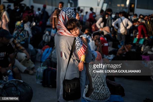 Woman holds her child as refugees from the islands of Lesbos, Chios, Samos, Kos and Leros wait to board buses after disembarking at the port of...