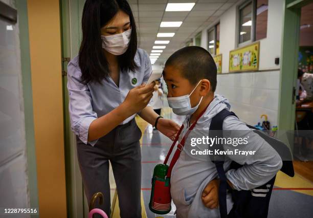 Chinese teacher checks the temperature of a student wearing a protective mask as he arrives for classes at Chaoyang Experimental Primary School on...