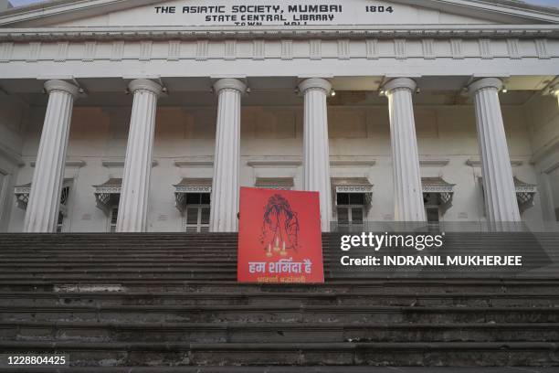 Social activist places a hoarding before a vigil following accusations of Indian Police forcibly cremating the body of a 19-year-old woman victim,...