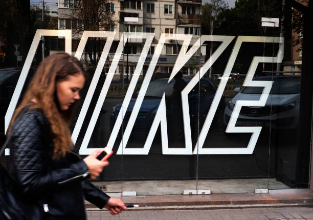 Woman with a smartphone walks past the Nike logo at one of their branches.