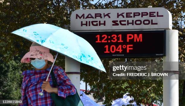 The temperature reads 104F degrees at Mark Keppel High School in Monterey Park, California, as a masked pedestrian uses an umbrella for shade on...