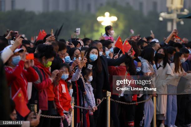 People wearing face masks watch the flag-raising ceremony at Tiananmen Square to mark the 71st Anniversary of the Founding of the People's Republic...