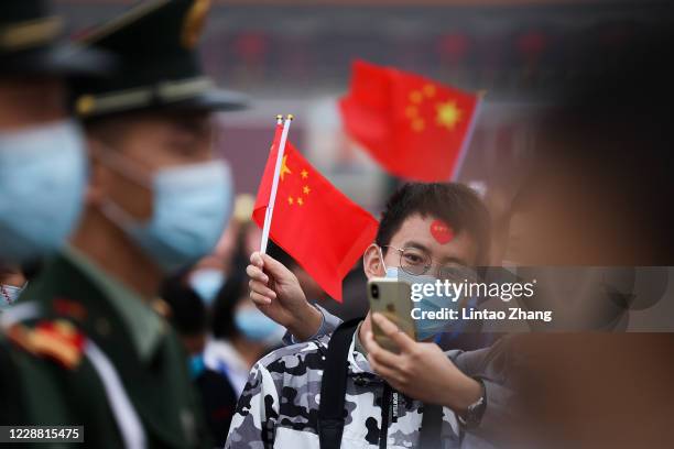 People wearing face masks watch the flag-raising ceremony at Tiananmen Square to mark the 71st Anniversary of the Founding of the People's Republic...
