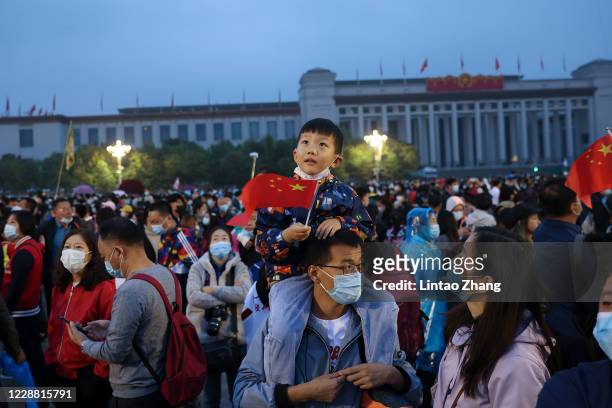 Child holds a national flag as he sits on the shoulders of a man as they watch the flag-raising ceremony at Tiananmen Square to mark the 71st...