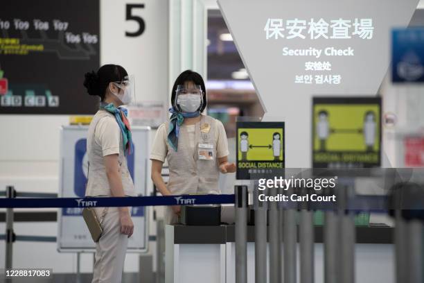 Staff members wearing face masks and plastic visors wait at the security check at Haneda Airport on October 1, 2020 in Tokyo, Japan. Japan recently...