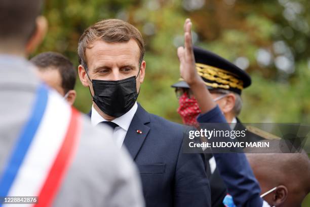 French President Emmanuel Macron wearing a protective face mask speaks watches a child as he arrives at 'la Maison des habitants' to meet and have...