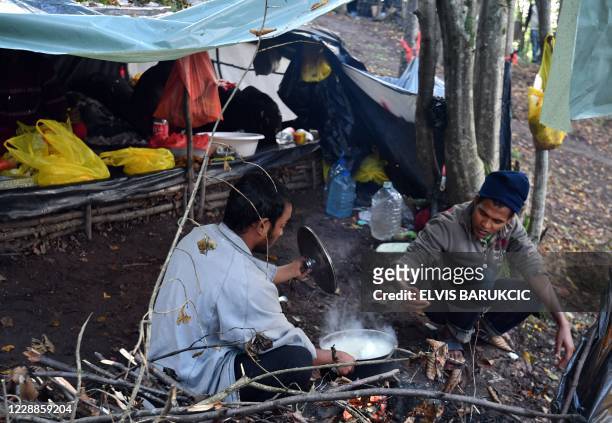 Migrants from Bangladesh, awaiting to enter Croatia, cook and warm up near a fire at an improvised camp in the woods, hundreds of meters away from...