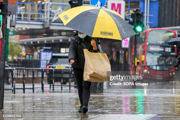 Shopper wearing a face mask shelters from the rain underneath an umbrella on a wet and windy day caused by Storm Alex.