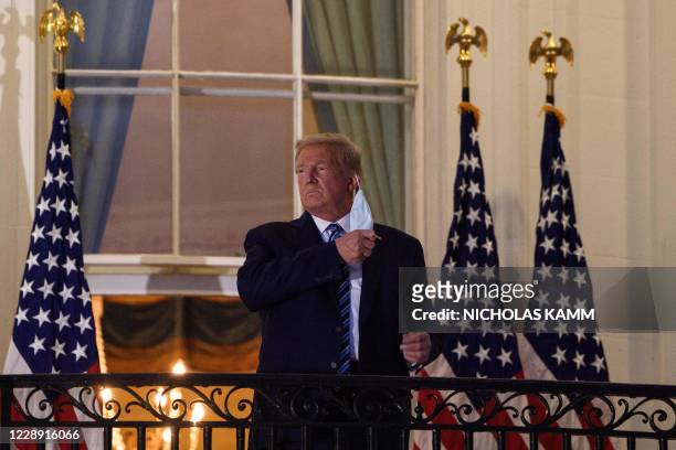 President Donald Trump takes off his facemask as he arrives at the White House upon his return from Walter Reed Medical Center, where he underwent...