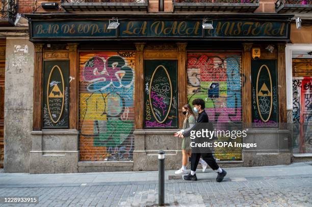 People wearing face masks walking past a closed bar in the Malasaña neighborhood. The Community of Madrid requires the Spanish Government to suspend...