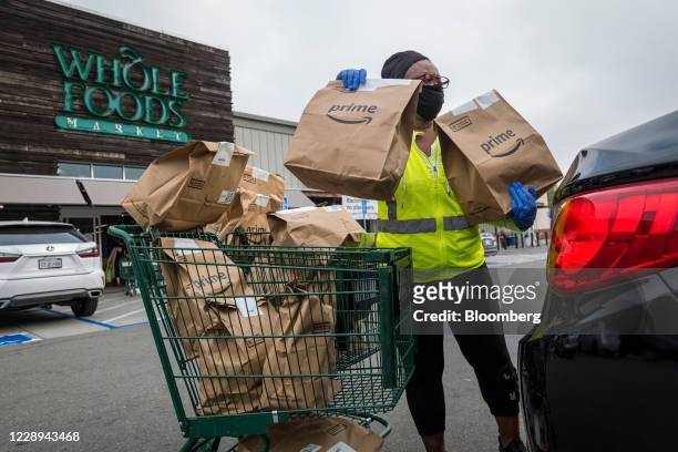 An independent contractor wearing a protective mask and gloves loads Amazon Prime grocery bags into a car outside a Whole Foods Market in Berkeley,...