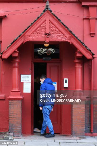 Customer wearing a face mask or covering due to the COVID-19 pandemic, passes a hand sanitising unit as he enters a pub in Liverpool, north west...