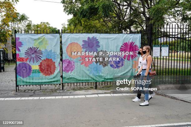 People wearing face masks walk past a Marsha P. Johnson State Park banner in Williamsburg.