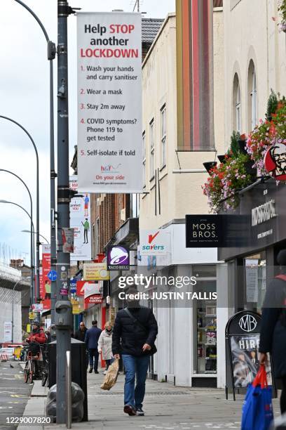 Pedestrian wearing a face mask as a precaution against the transmission of the novel coronavirus, walks beneath a sign reminding members of the...