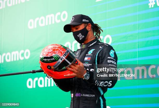 Winner Mercedes' British driver Lewis Hamilton holds the red helmet of former German Formula one champion Michael Schumacher that was offered to him...