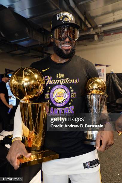 LeBron James of the Los Angeles Lakers holds the Larry O'Brien Championship Trophy and the Bill Russell NBA Finals Most Valuable Player Trophy after...