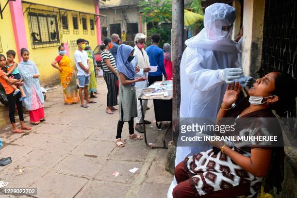 Health worker wearing protective gear collects a swab sample from a resident during a Covid-19 coronavirus screening at a civic clinic in Dharavi...